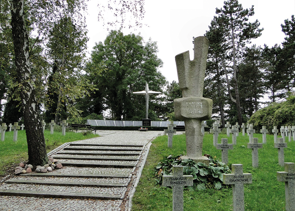 Współczesna fotografia przedstawiająca Kwaterę Pionierów na Cmentarzu Centralnym w Szczecinie. Na pierwszym planie widoczne są rzędy betonowych krzyży nagrobnych z wyrytymi nazwiskami pierwszych polskich mieszkańców miasta. Po prawej stronie stoi masywny, kamienny obelisk z napisem: „KWATERA PIONIERÓW SZCZECIŃSKICH 1945-1946”. Szeroka, brukowana aleja ze schodami prowadzi w głąb kwatery, gdzie na tle wysokich drzew wznosi się wysoki, metalowy krzyż oraz ściana z pamiątkowymi tablicami.